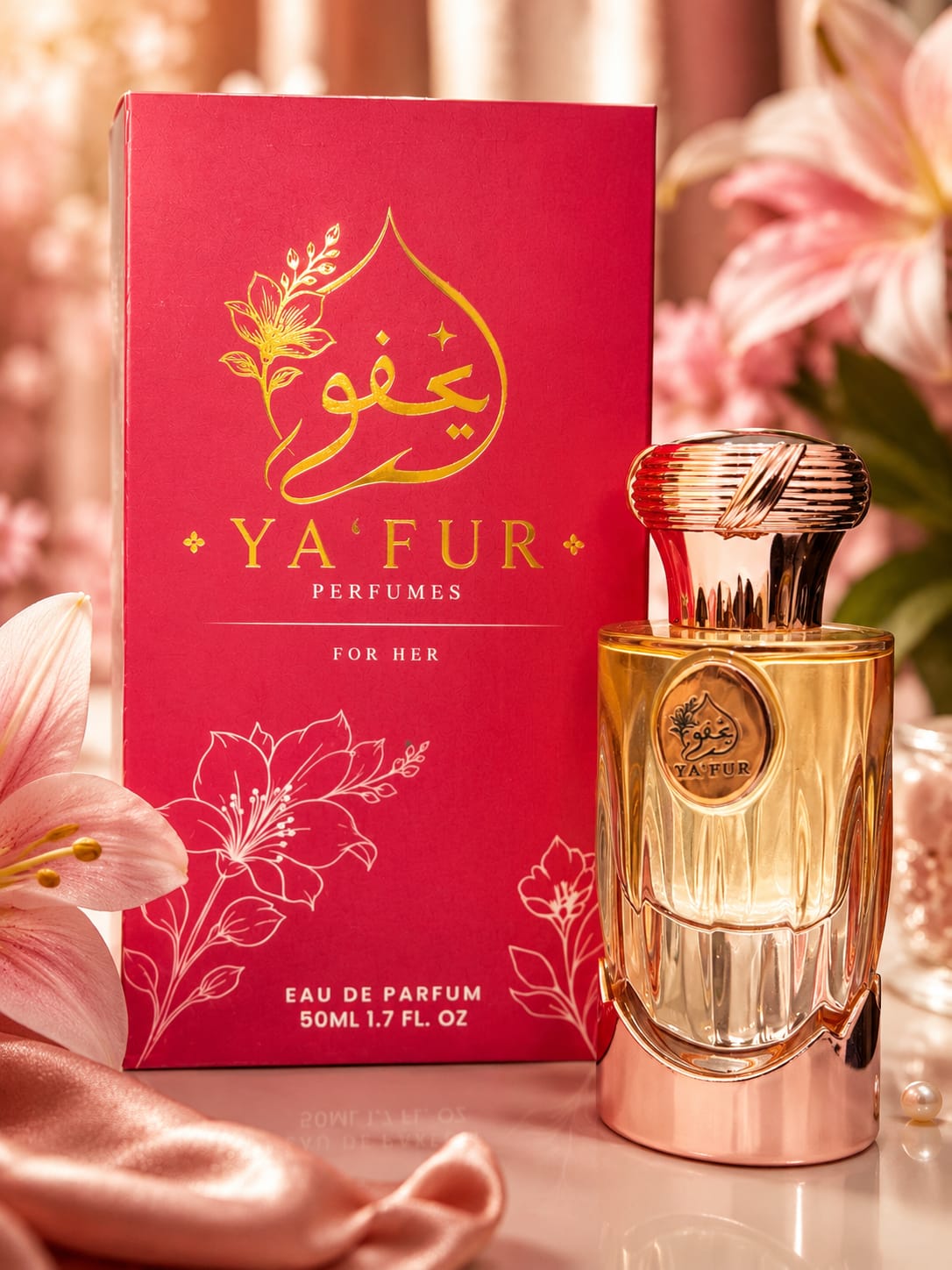 A bottle of YA'FUR PERFUMES Eau de Parfum next to its red and gold packaging box, styled with pink lilies and draped satin fabric.